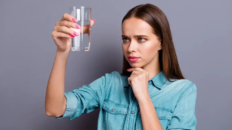 Дівчина тримає склянку з водою та міркує чи вона безпечна