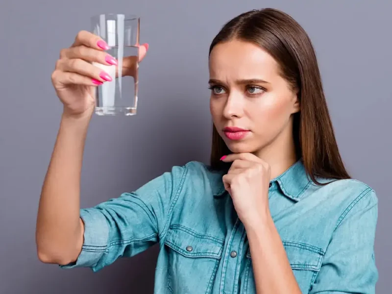 Дівчина тримає склянку з водою та міркує чи вона безпечна