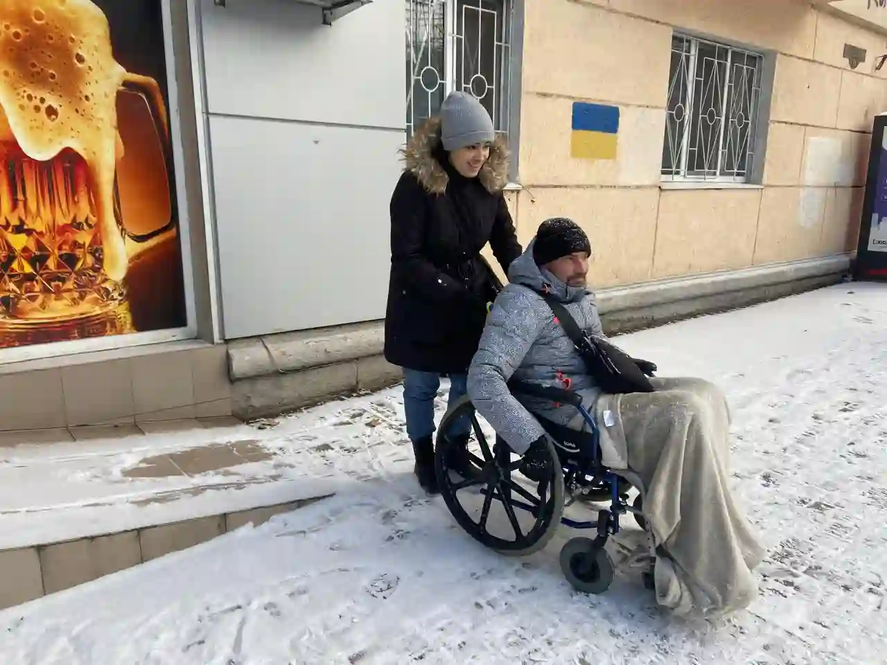 Жінка допомогає чоловіку у кріслі колісному