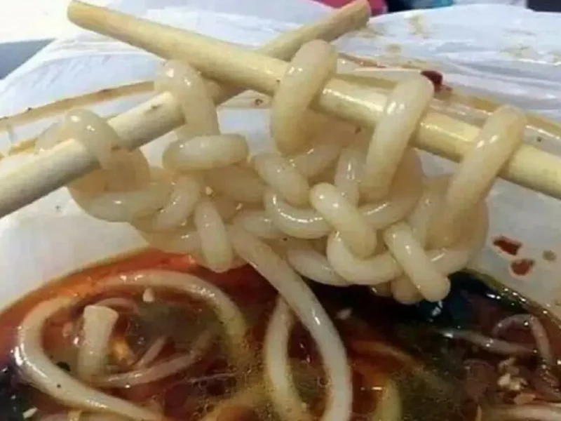 Тарелка азиатской лапши, которая аккуратно связана в узлы, имитирующие вязание крючком, с палочками для еды