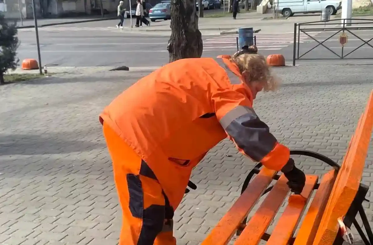 Співробітниця ЖКС фарбує скамійку