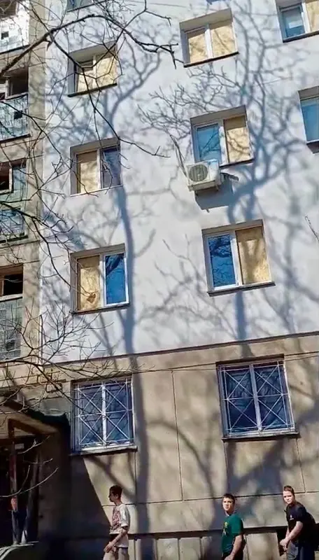 Фасад багатоповерхового будинку в Хаджибейському районі Одеси, де більшість вікон забиті фанерою після атаки дронів. На передньому плані видно місцевих жителів