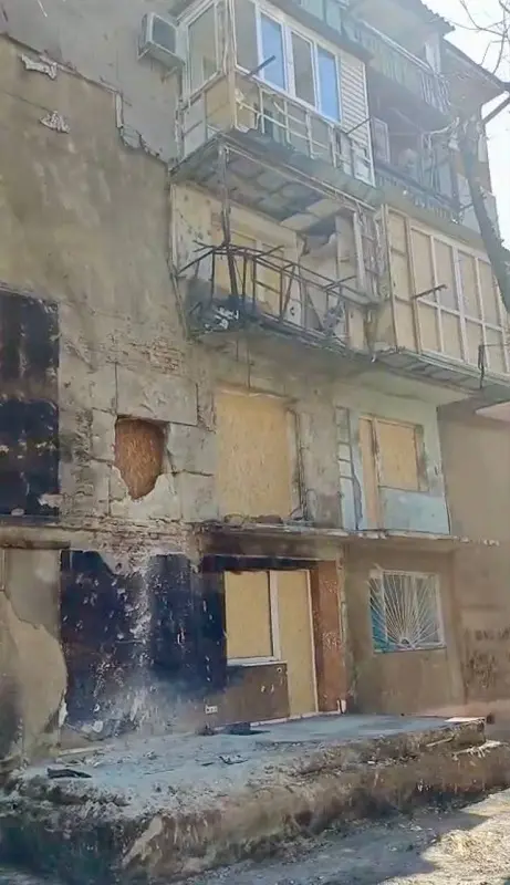 Великий план пошкодженого фасаду житлового будинку в Одесі. Видно сліди пожежі, наскрізні дірки в стінах, зруйновані балконні решітки та забиті фанерою віконні отвори