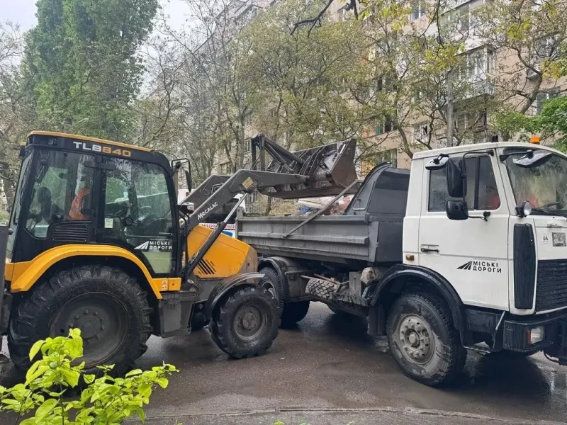 Спецтехника КП «Городские дороги» убирает строительный мусор после обстрела в Одессе. Погрузчик засыпает обломки в кузов грузового автомобиля на фоне жилой застройки