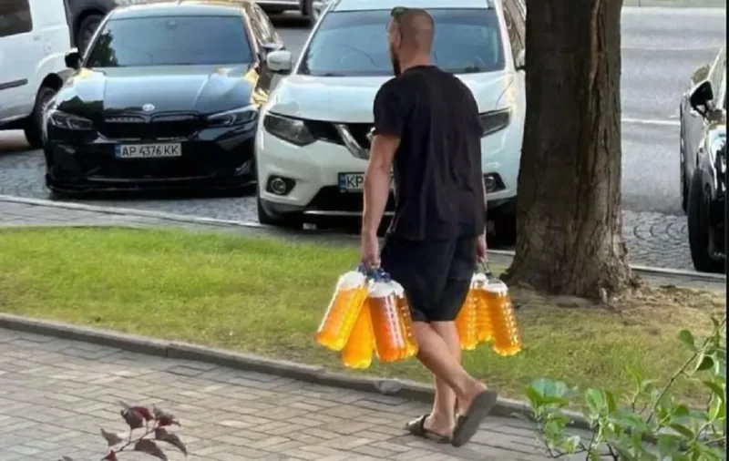 Мужчина идет по улице и несет в руках 4 пятилитровые баклаги с пивом