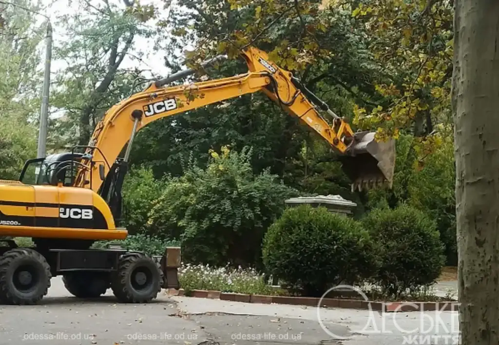 Желтый экскаватор JCB заносит ковш над каменным постаментом демонтированного бюста Мичурина на территории Селекционного института в Одессе